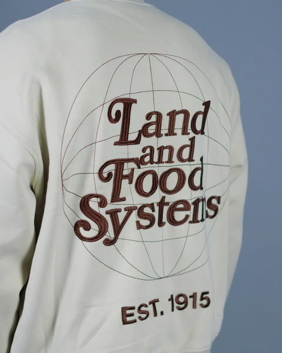 The back of a cream crewneck embroidered Land and Food Systems, Est. 1915